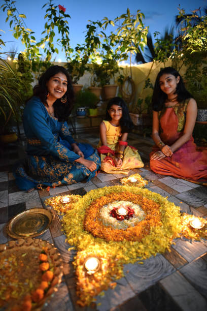 istock Mother and daughters lighting lamps around rangoli made using petals 1277474818