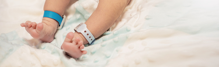 Closeup feet of newborn baby with tag on the legs in hospital bed. Healthcare and medical love lifestyle father or motherâs day background concept banner