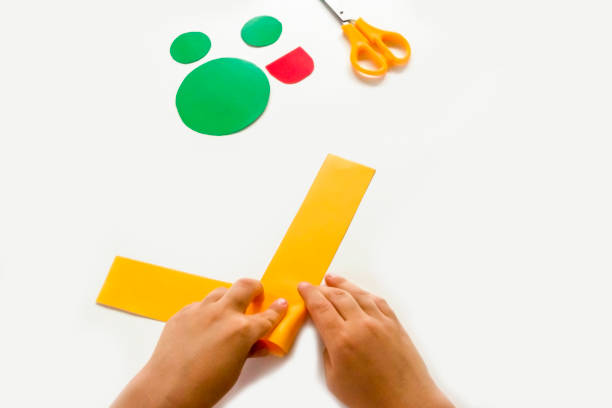 istock Concept of DIY and children's creativity. Step by step instruction: how to make applique frog from paper. Step 3 child bends the paper. Selective focus, artificial noise, clipping path 1277477573
