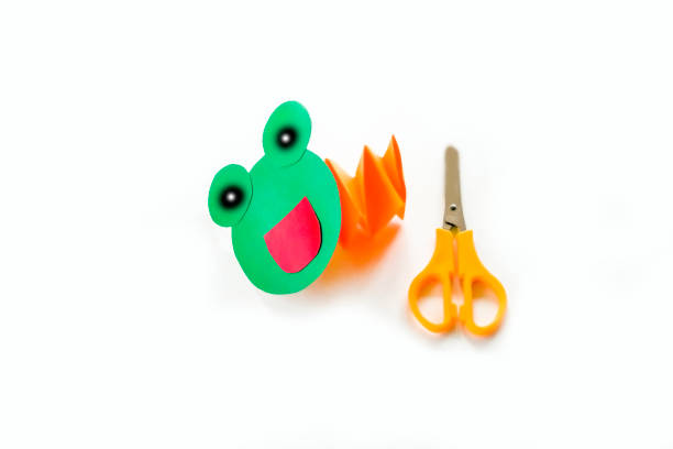 istock Concept of DIY and children's creativity. Step by step instruction: how to make applique frog from paper. Step 6 finished result - paper frog on spring.  Selective focus, artificial noise, clipping path 1277477595