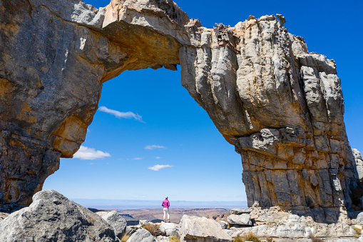 A fit woman hiking in the Cederberg Mountains near Cape Town. Woman stands below the Wolfberg Arch and admires the view over the extreme terrain. Iconic mountain range in South Africa