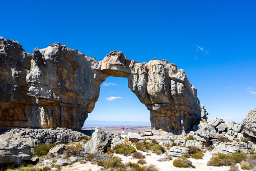 A fit woman hiking in the Cederberg Mountains near Cape Town. Woman stands below the Wolfberg Arch and admires the view over the extreme terrain. Iconic mountain range in South Africa
