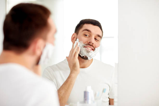 istock happy man applying shaving foam at bathroom mirror 1277481700