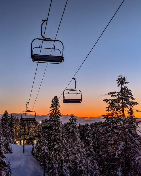 telesilla vacía en una estación de esquí cerrada durante una puesta de sol naranja, grouse mountain, vancouver, columbia británica, canadá - telesilla fotografías e imágenes de stock