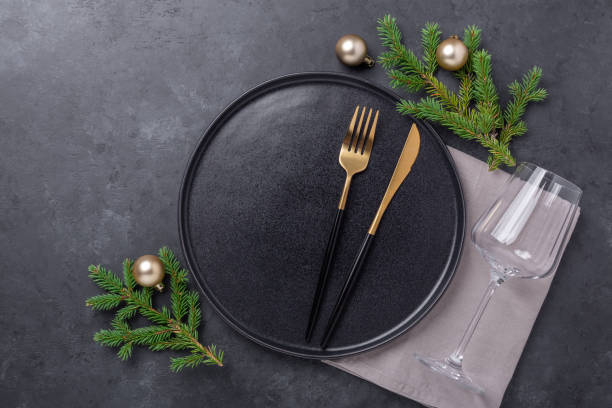 istock Christmas table setting with empty black ceramic plate, fir tree branch and gold accessories on black stone background. Top view. Copy space 1277482221