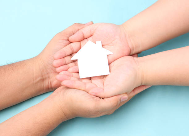 istock hands holding paper house on blue background. 1277482838