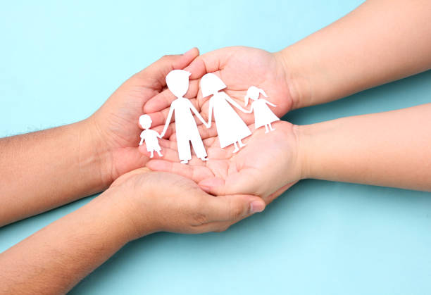 istock hands holding paper family cutout on blue background. 1277482844