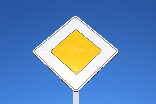 Traffic sign begin of a priority road. A yellow rhombus with a white border and reflective coating against a clear blue sky