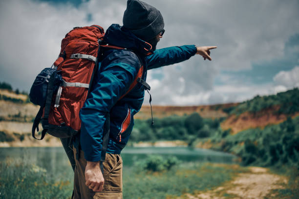 istock Rear view of handsome bearded man with backpack pointing something on camping trip. 1277495595