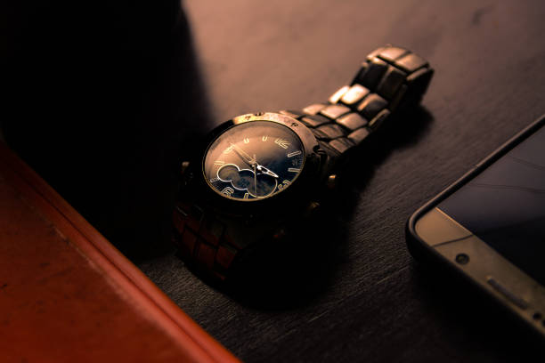 old metallic wrist watch and broken screen mobile phone in dark moody light