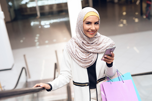 Beautiful arab girl with a phone in her hands looks at the camera and holds packages in her hands. Girl in arabic clothes came to the mall for shopping.