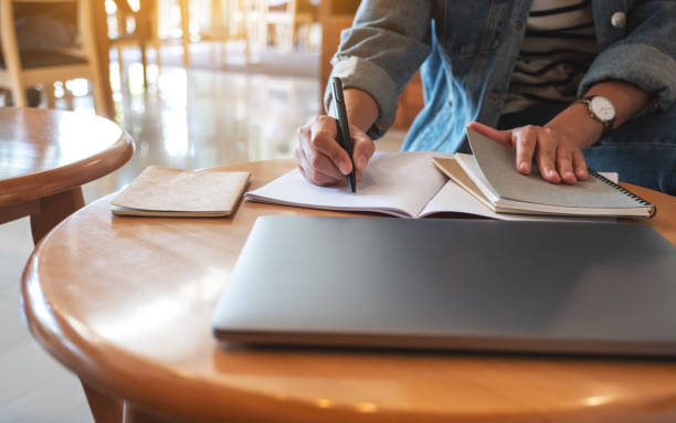istock a woman writing on a notebook with laptop computer on the table 1277500368
