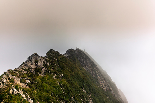 Fog and clouds enveloping a clmber on the steep ridge of the majestic Schaefler peak in the Alpstein mountain range in Appenzell