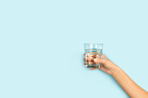 Woman hand holding a glass of water on a light blue background