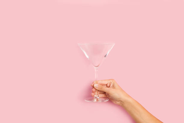 рука женщины держа пустой стеколь коктейля на розовом фоне - martini cocktail martini glass glass стоковые фото и изображения