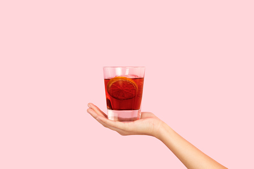 Woman hand holding a glass of red vermouth on a pink background