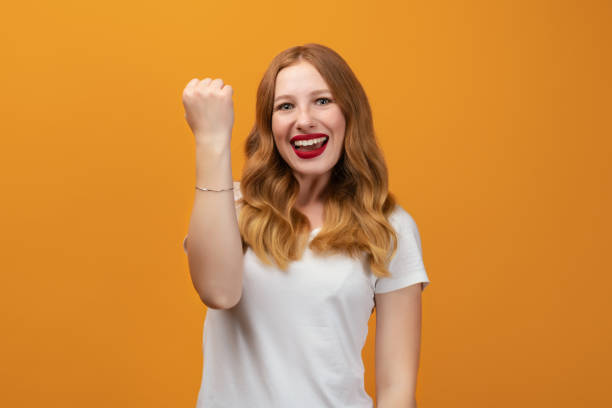 istock Successful girl with long wavy redhead, making Winner gesture, standing yellow background 1277508654