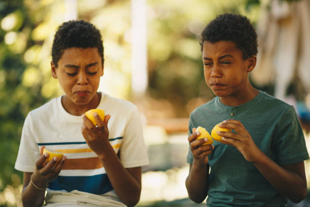 istock Two brothers african ethnicity sitting outdoors and tasting lemon. 1277512045