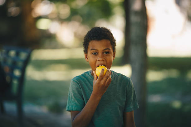 istock Little african boy standing outdoors and tasting lemon. It's a beautiful summer sunny day outside. 1277512287
