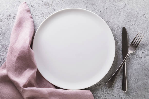 istock Empty ceramic plate white, napkin and cutlery on the table with concrete texture, top view. Food background 1277512739