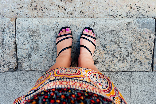 woman's feet in first person view with fuchsia painted nails and black shoes, in Moroccan tribal dress, on gray stone tiles. ethnicity concept