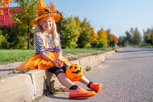 Halloween kids. smiling girl in witch hat with pumpkin candy bucket. Funny kids in carnival costumes outdoors.