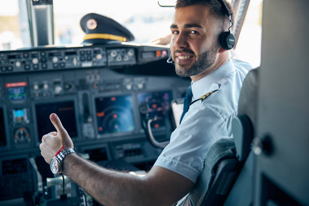 Handsome male posing at the camera in cabin of passenger aircraft Close up portrait of beaming smiling man pilot in uniform showing like while he is sitting on the chair in cockpit of civil airplane throttle photos stock pictures, royalty-free photos & images