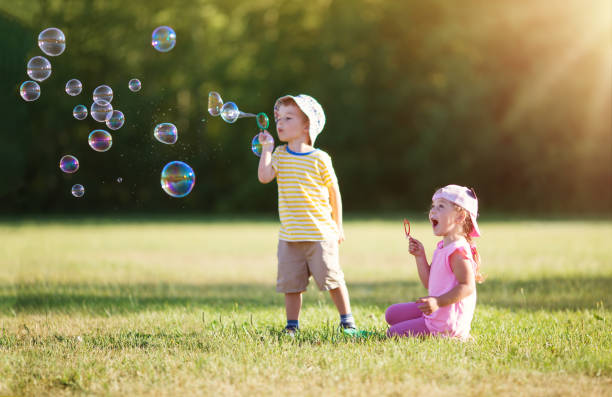 Happy children having fun in grass on sunny summer evening. Kids outdoors in nature blowing bubbles.