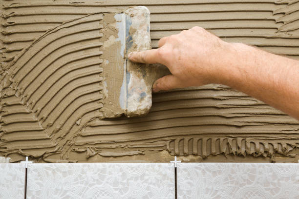 istock Worker hand using spatula and putting glue on wall. Gluing ceramic tiles. Closeup. 1277534165