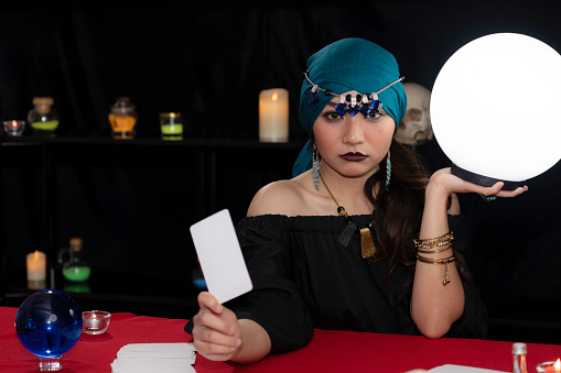 Beautiful fortune-teller in a black dress holding a white crystal ball and tarot cards used to predict fortunes.