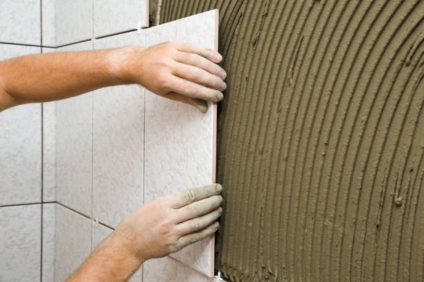 istock Worker hands gluing ceramic tiles on wall. Closeup. Side view. 1277535378