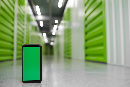 Background image of storage facility with green screen smartphone in foreground, copy space
