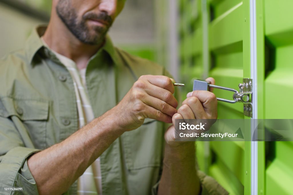 Man Opening Storage Unit Close up of handsome man opening padlock on door of self storage unit , copy space Self Storage Stock Photo