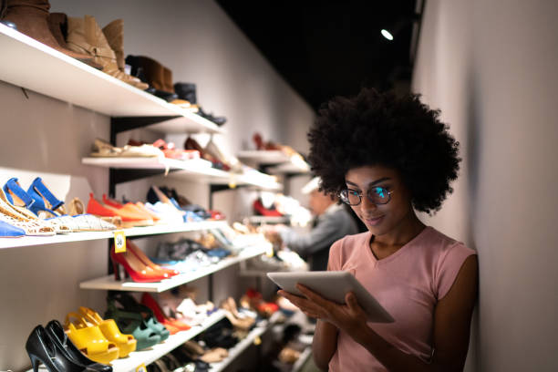 jeune femme utilisant la tablette numérique pour enregistrer invetory à un magasin de chaussures - commerçant photos et images de collection