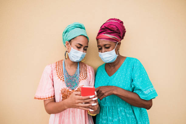 African mother and daughter with smartphone while wearing protective face mask for coronavirus