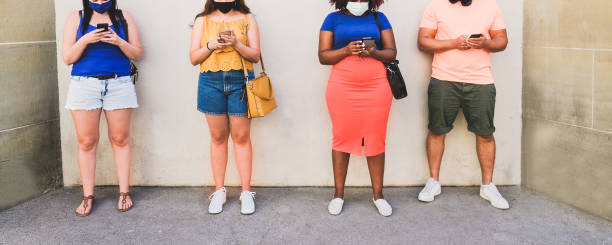istock Multiracial people standing in a line looking at smartphone while wearing protective face mask for coronavirus 1277539807