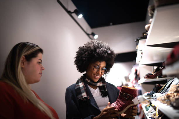 młoda kobieta jest wspomagana przez sprzedawczyni podczas zakupów butów w sklepie oszczędności - shoe store sales clerk customer zdjęcia i obrazy z banku zdjęć