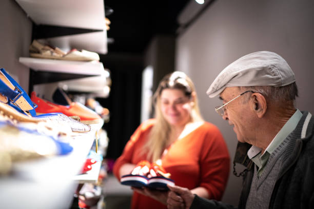 starszy mężczyzna jest wspomagany przez sprzedawczynię podczas zakupów butów w sklepie oszczędnościowym - shoe store sales clerk customer zdjęcia i obrazy z banku zdjęć