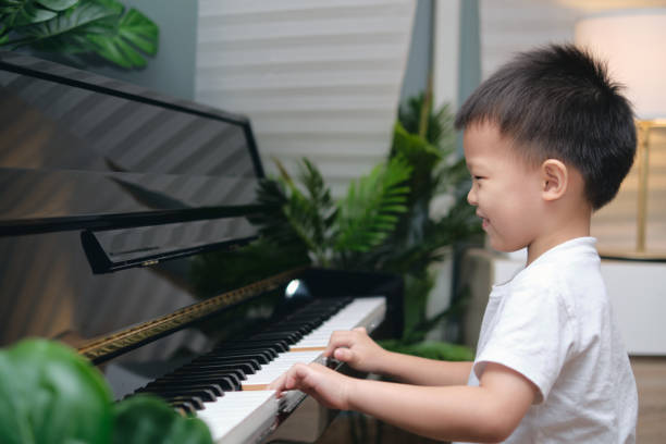 carino felice sorridente bambino asiatico ragazzo che suona il pianoforte in soggiorno a casa, bambino in età prescolare che si diverte con l'imparare a suonare lo strumento musicale - toddler music asian ethnicity child foto e immagini stock