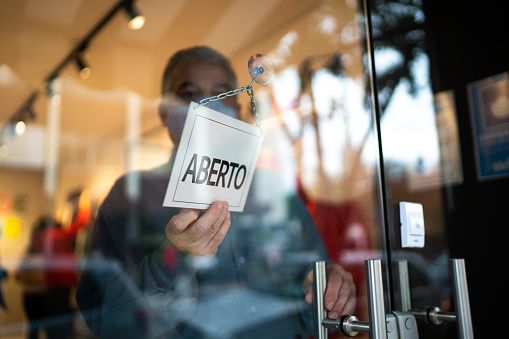 Business ower holding turning sign (aberto in Portuguese) on storefront door