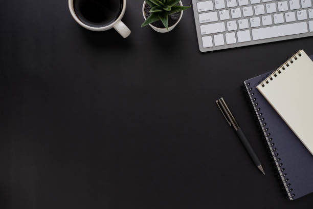 istock Top view above of Black office desk table with keyboard, notebook and coffee cup with equipment other office supplies. Business and finance concept. Workplace, Flat lay with blank copy space. 1277547120