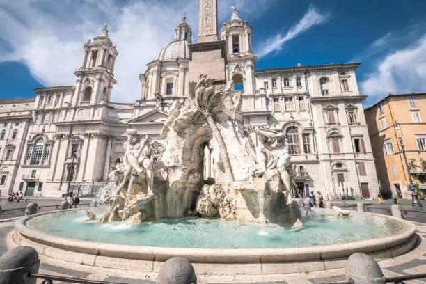 View of the beautiful fountain of the four rivers, Navona square in Rome Italy. Ancient obelisk and Sant'Agnese church, blue sky and clouds in background. Few tourists due to the covid 19 pandemia.