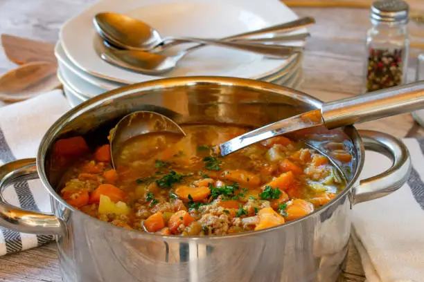 fresh cooked carrot soup with minced meat served in a big pot with ladle on a table - ready to eat