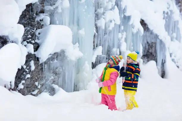 Photo of Children play with icicle in snow. Kids winter fun
