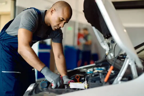 Photo of African American mechanic repairing car engine in a workshop.