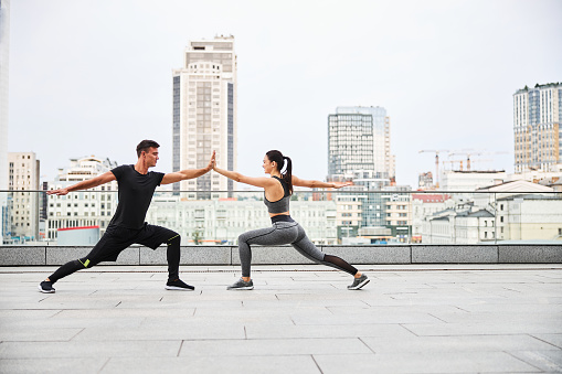 Smiling athletic male and female are practicing yoga together on top terrace of urban building