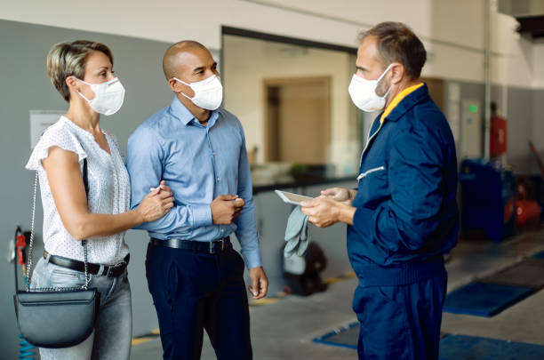 pareja y reparador de automóviles que usan máscaras protectoras para la cara mientras hablan en un taller. - auto repair shop mechanic digital tablet customer fotografías e imágenes de stock