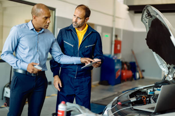 mid adult mechanic y su cliente usando touchpad en el taller de reparación de automóviles. - auto repair shop mechanic digital tablet customer fotografías e imágenes de stock