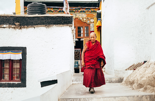 Thiksay Monastery in Thiksey village, India â August 20, 2016: Aged monk goes by the monastery weared in traditional red kasaya  in Thiksey village, India