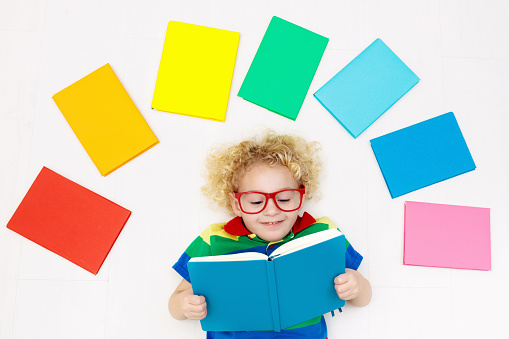 Little boy with colorful rainbow books. Happy back to school student. Child reading and doing homework. Preschooler kids learn and read a book. Curly funny kid in elementary school or kindergarten.